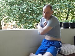 Man undressing outside on the balcony naked he wanks his semi-erect shaved cock becoming erect and gets dressed again